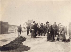 Photo Credit: The Rooms Provincial Archives VA 104-22.1; Royal salute or feu de joie for a wedding party at Harrington Harbour. International Grenfell Association photograph collection. Note the men with the guns in the background.